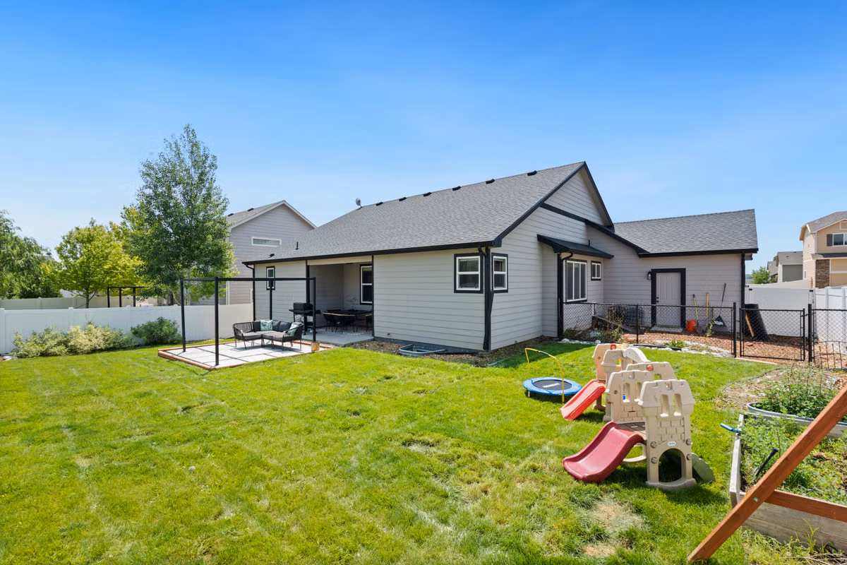 A peaceful suburban backyard featuring a children's play area and a cozy patio under a clear blue sky.